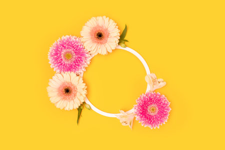 Round frame made of green leaves, alstroemeria and gerbera flowers on a yellow background.の写真素材