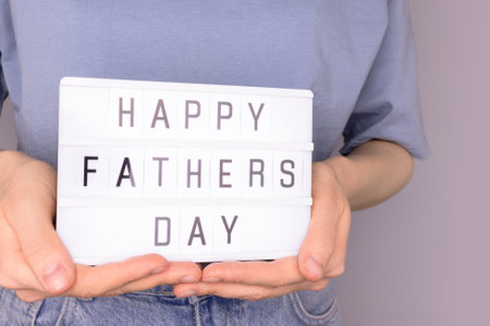 Happy Fathers Day. Female hands hold lightbox with letters in front of blue background. Festive concept.の写真素材