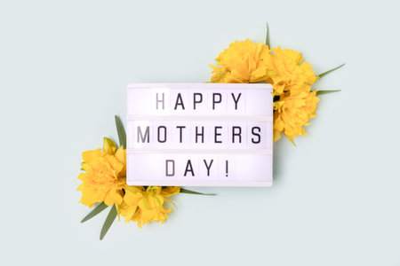 Happy Mothers Day. Lightbox with quote and frame made of yellow narcissus on a blue pastel background.の写真素材