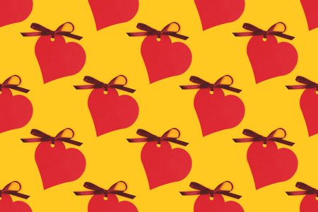 Pattern made of red empty tags in a heart shape with tied ribbon bow on a yellow background.の写真素材