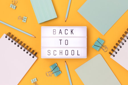 Back to school. Lightbox with letters and frame made of mint colored stationery on a yellow background.の写真素材