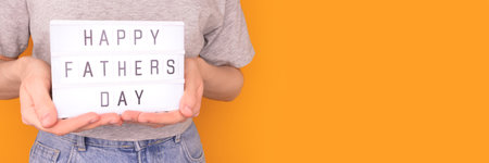 Happy Fathers Day. Banner with woman hold in hands lightbox with letters in front of yellow background. Festive concept.の写真素材