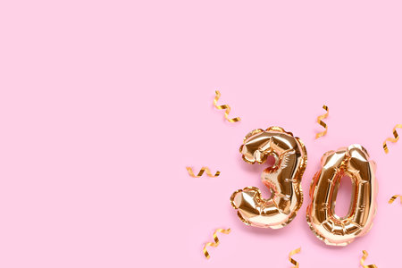 Number 30 gold air balloons with ribbon confetti on a pink background with copy space.の写真素材