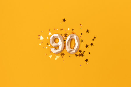Gold colored number 90 and stars confetti on a yellow background. Festive glowing compisition.の写真素材