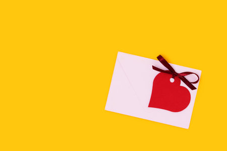 Red empty tag in a heart shape with tied ribbon bow and envelope on a yellow background.の写真素材
