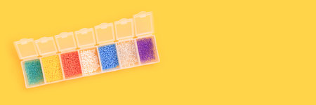Banner with multicolored beads in a storage container on a yellow background.の写真素材