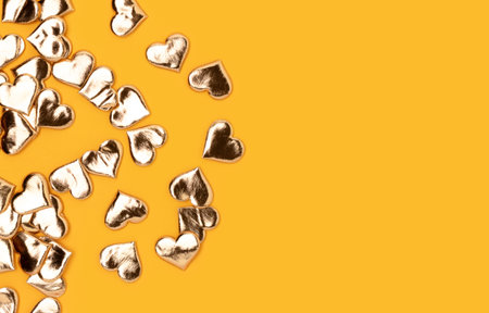 Gold colored hearts confetti on a yellow background. Holidays concept with copy space.の写真素材