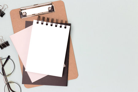 Workspace with blank notepad mockup, eyeglasses and stationery on a blue background. Office supplies.の写真素材