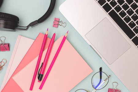 Workspace with laptop, eyeglasses and pink colored office supplies on a blue background. Online work concept.の写真素材