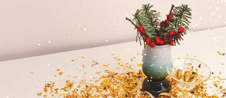 Banner with nobilis fir and winterberry branches in a vase, crystal glass and golden confetti in front of beige background.の写真素材
