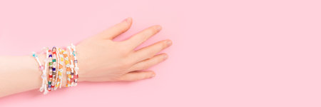 Banner with female hand with a lot of bracelets on it. Trendy jewelry made of pearls and beads on a pink background.の写真素材