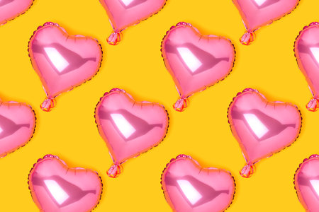 Repetitive pattern made of pink inflatable foil balloons in a heart shape. Festive concept on a yellow background.の写真素材