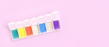 Banner with multicolored beads in a storage container on a purple background. Place for text.