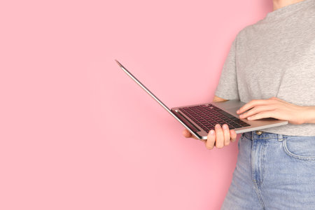 Woman hold in hands laptop. Remote work concept in front of pink pastel background.の写真素材