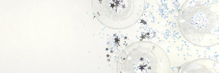 Banner with crystal glasses and stars confetti on a silver glittering background. Festive composition.の写真素材