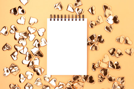 Empty notepad mockup with gold colored hearts confetti. Festive concept.の写真素材