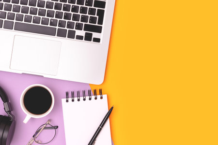 Workspace with laptop, eyeglasses and stationery on a purple and yellow background. Place for text.