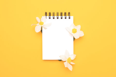 Clean notepad mockup with white narcissus flowers on a yellow background. Place for text.の写真素材