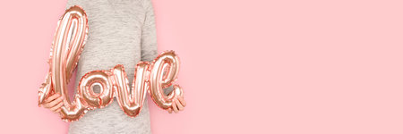 Banner with woman in a gray dress hold in hands inflatable foil balloon. Word Love in front of pink background. Place for text.の写真素材