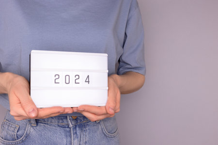 Female hands hold lightbox with 2024 numbers in front of blue background. New Year concept with copy space.の写真素材