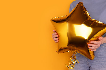 Woman hold in hands golden inflatable balloon in a star shape. Holidays concept in front of yellow background.の写真素材