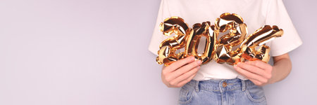 Banner with 2024 numbers. Hands hold a golden inflatable foil balloons in front of blue background.の写真素材