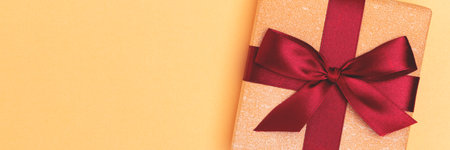 Banner with gift box with red ribbon on a golden shiny background. Festive concept with place for...