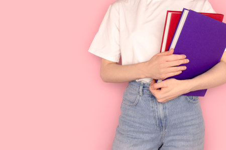 Unrecognizable woman holding books in her hands. Minimal concept with copy space in front of pink background.の写真素材