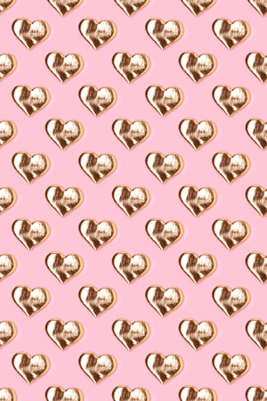 Repetitive pattern made of gold colored hearts. Creative layout on a pink background.の写真素材