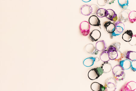 Multicolored handmade rings made of wire and natural stones scattered on a beige background. Place...