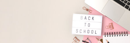 Banner with quote Back to school. Workspace with laptop and office supplies on a gray and pink...