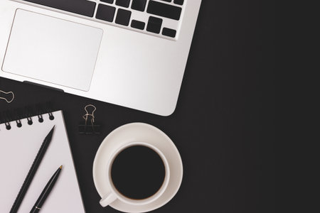 Workspace with laptop, cup of coffee and office supplies on a black background. Online studying...