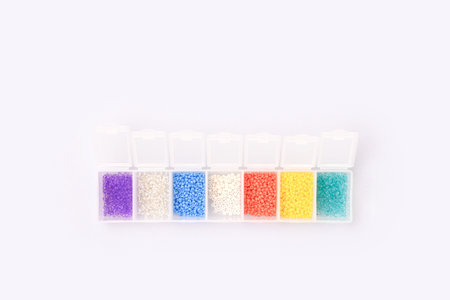 Multicolored beads in a storage container on a blue background. Leisure concept.