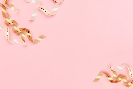 Gold colored ribbons scattered on a pink background with place for text. Selective focus.