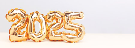 2025 New Year celebration banner. Golden foil balloons in front of blue and beige background.の写真素材