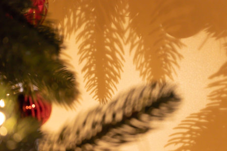 Defocused fir tree branches with red Christmas decorations. Shadows on a golden wall.の写真素材