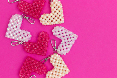 Handcracft keychains in a heart shape made from acrylic beads scattered on a magenta background....