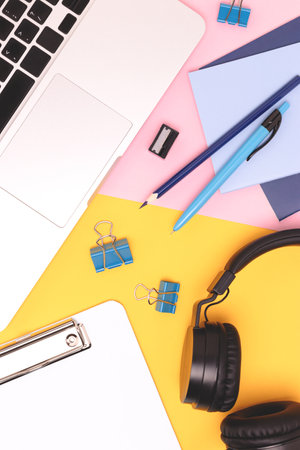 Workspace with laptop, headphones and office supplies on a pink and yellow background. Remote work concept.の写真素材