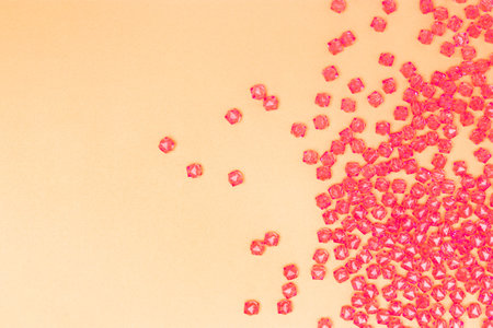 Pink acrylic beads scattered on a gold colored background with place for text.の写真素材