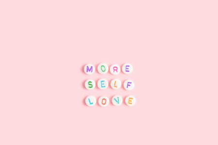 More self love. Quote made of white round beads with multicolored letters on a pink background.の写真素材