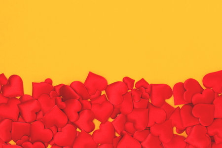 Red textile hearts confetti on a yellow background. Creative concept.