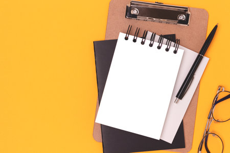 Workspace with blank notepad mockup, eyeglasses and stationery on a yellow background. Creative layout with place for text.の写真素材