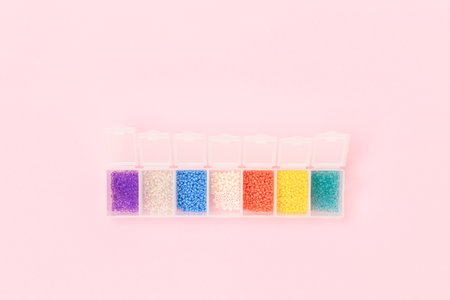 Multicolored beads in a storage container on a pink pastel background. Hobbies concept.の写真素材