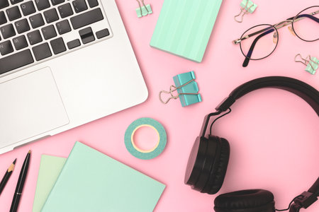 Workspace with laptop,headphones, eyeglasses and office supplies on a pink background. Workspace for...