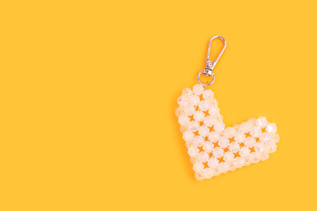 Keychain in a heart shape made from transparent shiny beads on a yellow background.