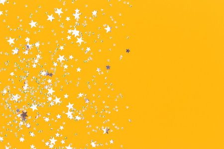 Silver stars and crystals confetti on a yellow background. Glowing concept with copy space.