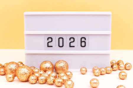 Creative New Year composition. Lightbox with 2026 numbers and sparkly balls in front of golden...