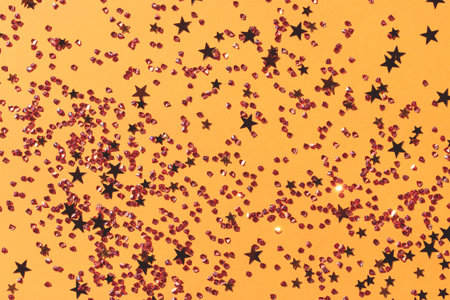 Gold colored stars and crystals confetti on a yellow background.の写真素材