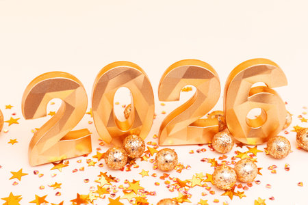 2026 - golden numbers and stars confetti on a beige background. New Year sparkly concept.