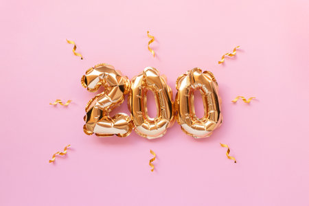 Number 200 golden air balloons with ribbons confetti on a pink background.の写真素材